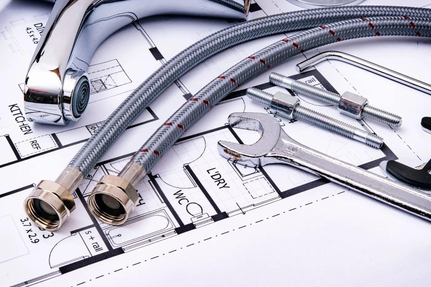 Chrome tap, braided hoses and a spanner lying on a house plan