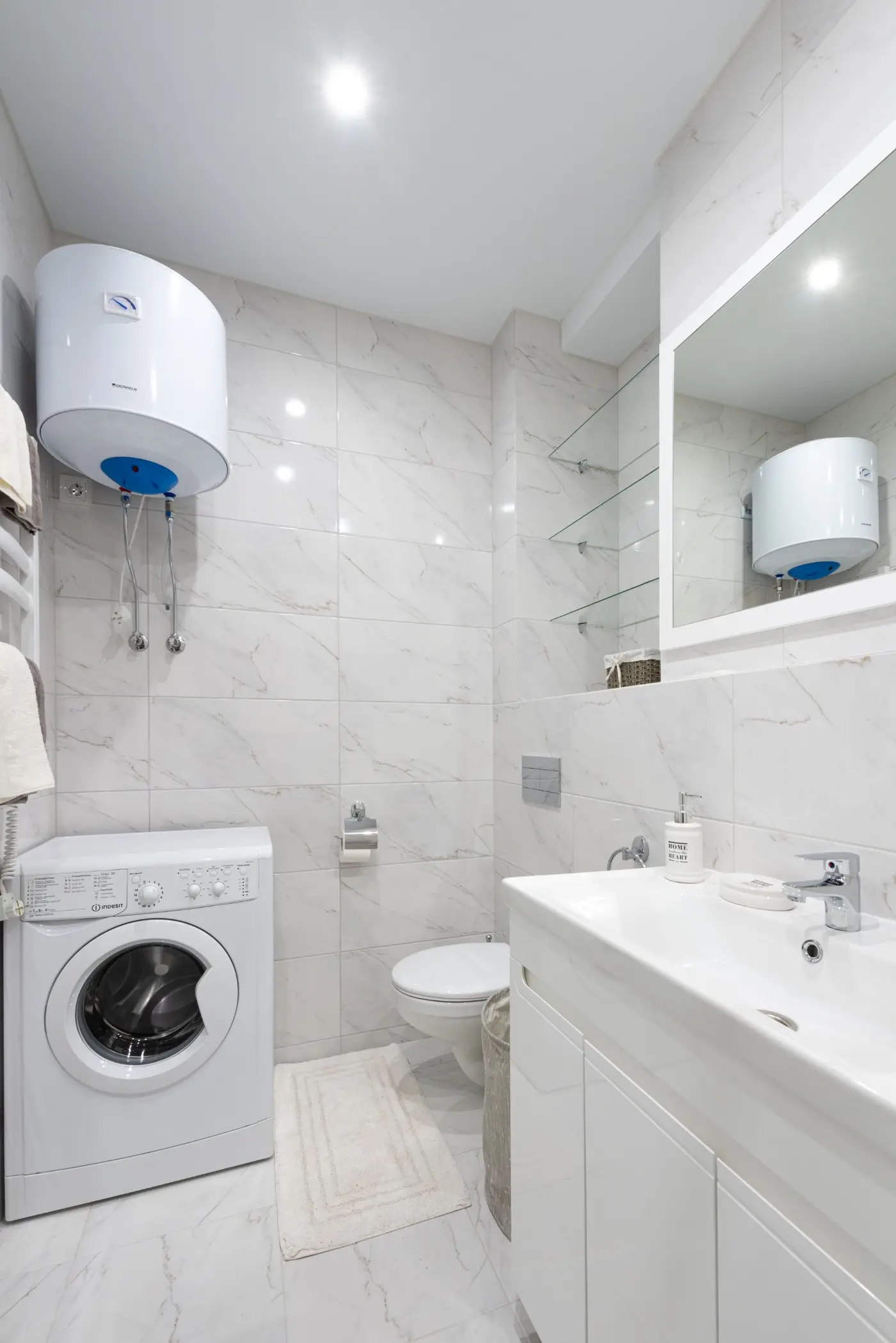 Electric geyser mounted on a bathroom wall above a washing machine