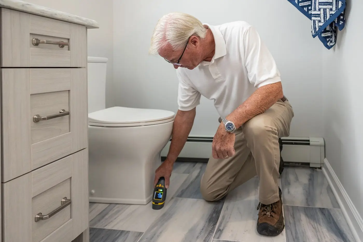 Plumber kneeling on a bathroom floor testing for a hidden leak with a meter