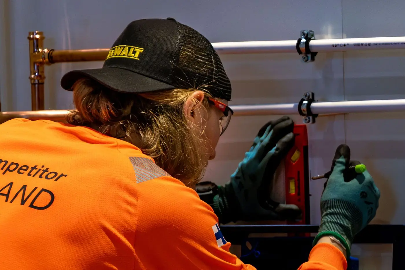Plumber in an orange work shirt connecting copper hot water pipes