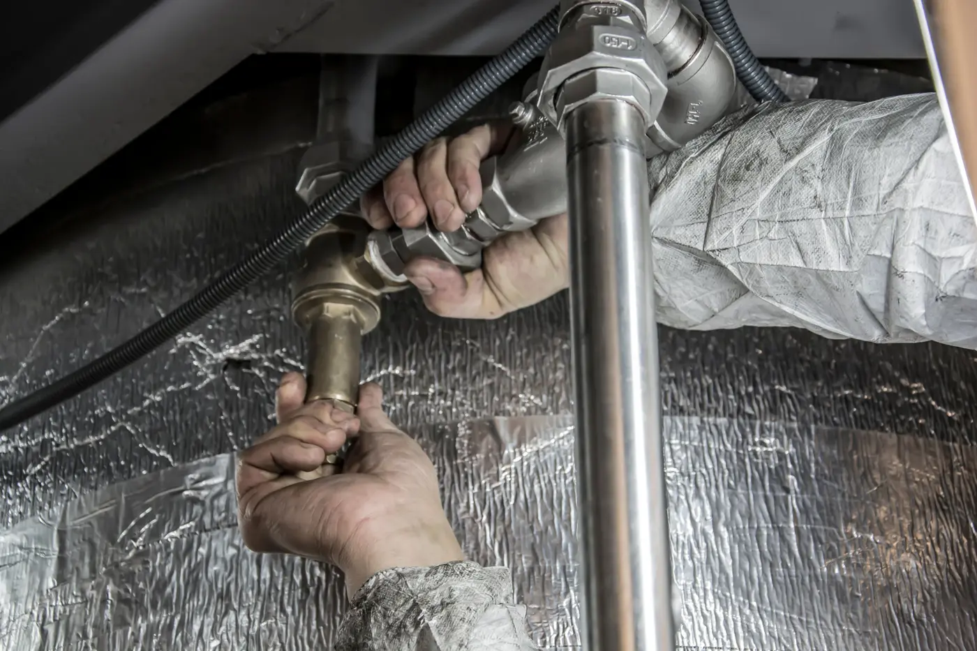 Plumber's hands tightening a brass valve under a sink